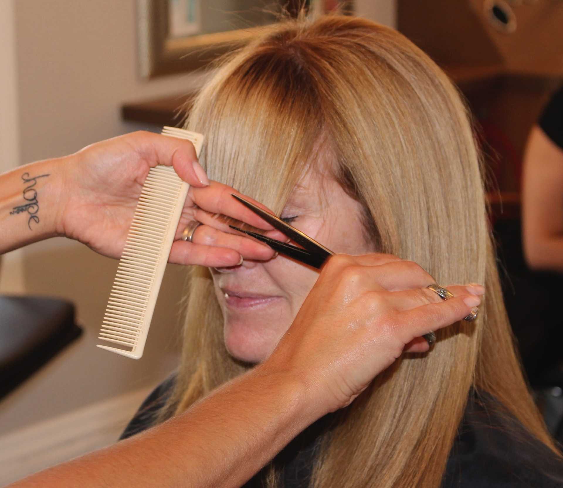 Hairdresser trims woman's bangs with scissors and comb in salon.