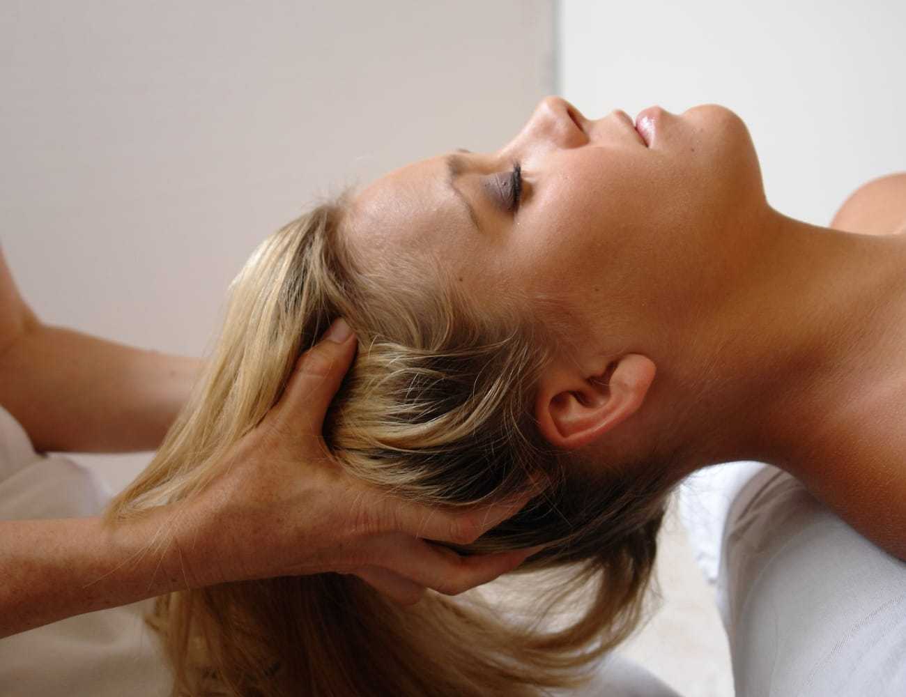 Head massage therapy session with a relaxed woman lying down.