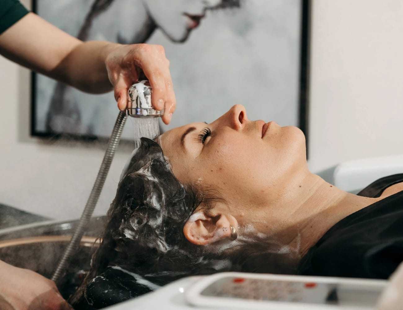 Woman receiving a hair wash at a salon, lying back while a stylist rinses her hair.